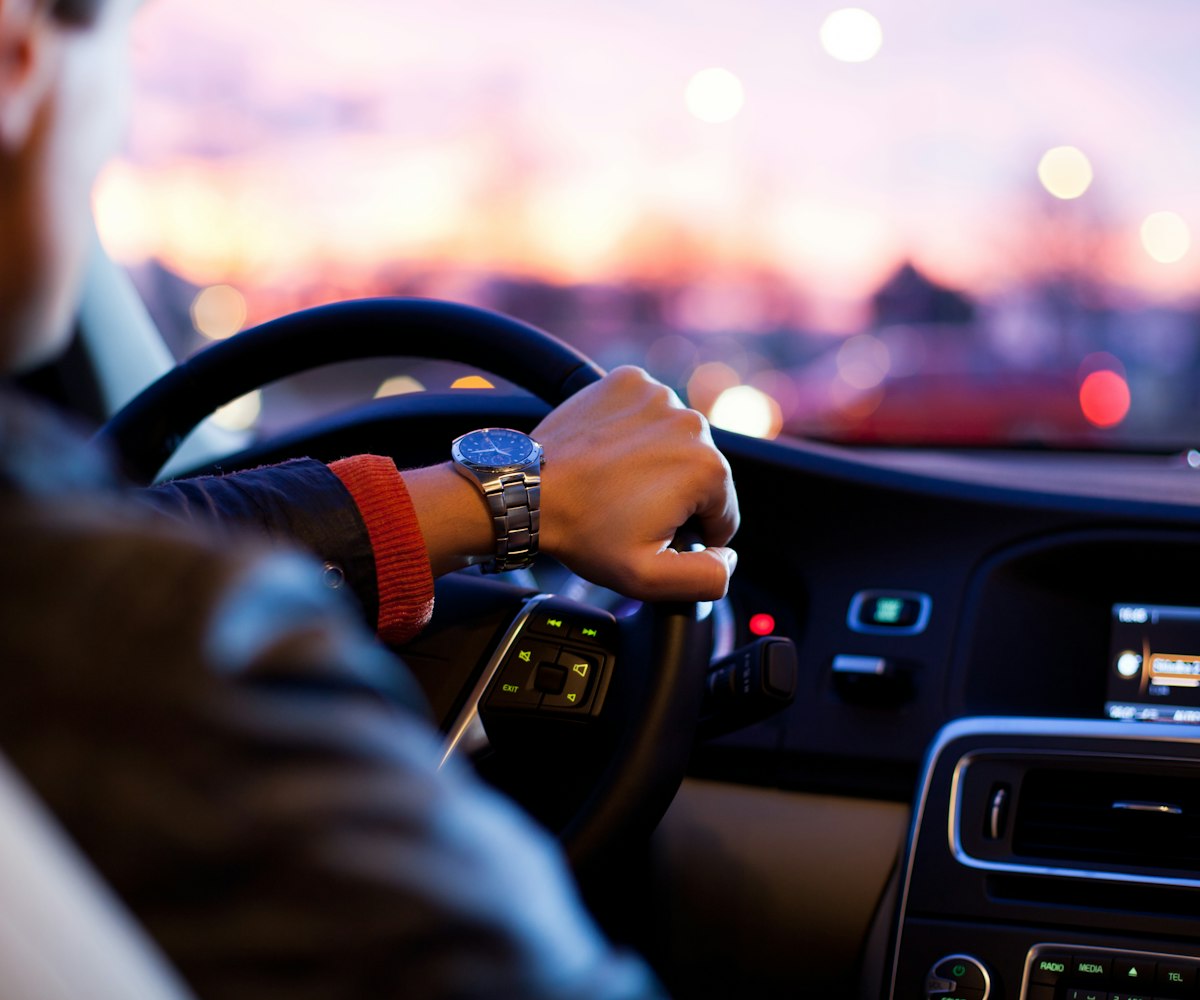 Driver behind the wheel of their own car at dusk, city lights ahead